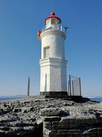 Lighthouse by sea against clear sky