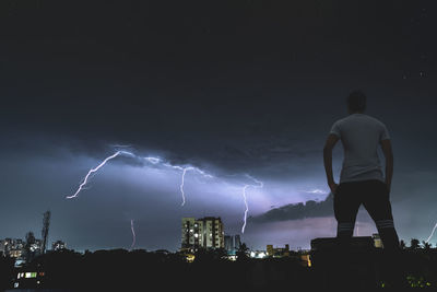 Rear view of silhouette man against illuminated cityscape against sky at night