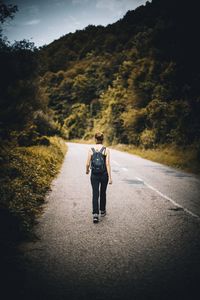 Rear view of man walking on road amidst trees
