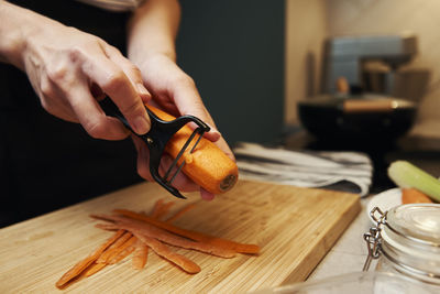 Woman scratchs carrot in kitchen, close up