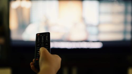 Cropped hand of person holding remote control while watching tv