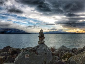 Man sitting on rock by sea against sky
