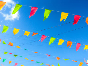 Low angle view of colorful bunting hanging against blue sky