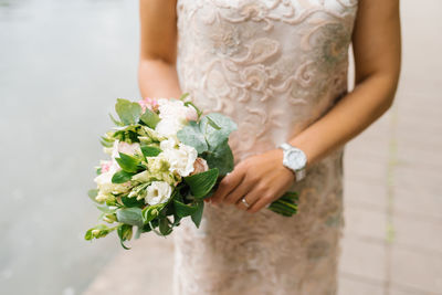 A bride in a beige wedding dress holds a bouquet of flowers and greenery in her hands