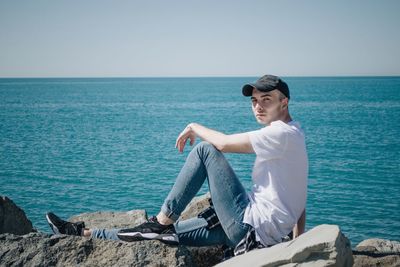 Full length portrait of man relaxing on rock against sea