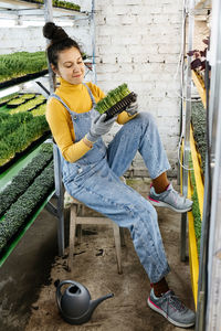 Young female farmer growing microgreens on her indoor vertical garden. happy woman looking 