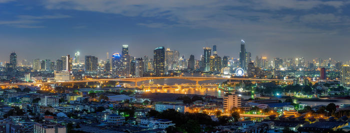 Illuminated buildings in city against cloudy sky