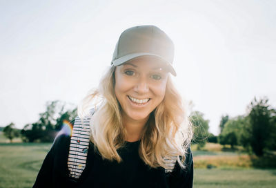 Portrait of a woman with tousled hair and a cap smiling in summer