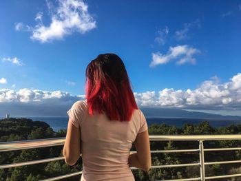 Rear view of woman standing by railing against sky