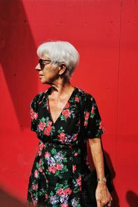 Woman looking away while standing against red wall