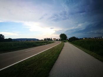 Empty road amidst field against sky