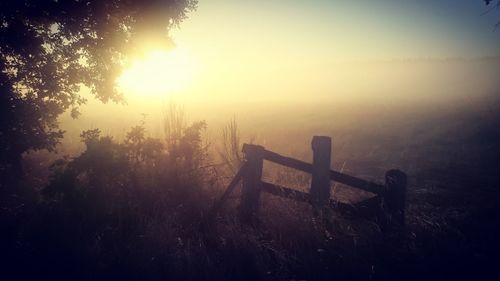 Fence on landscape against sky during sunset