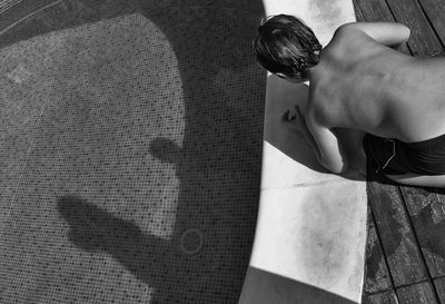 High angle view of shirtless boy kneeling on poolside