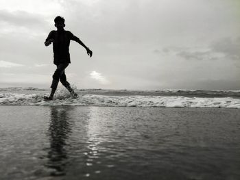 Man running on shore at beach against sky