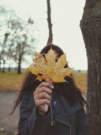 Woman holding maple leaf while standing outdoors