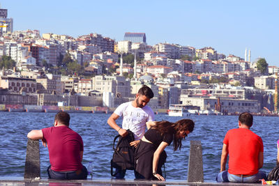 Rear view of people walking on sea against buildings in city