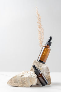 A brown cosmetic bottle with a pipette on astone stand on a gray background, with dried pampas grass