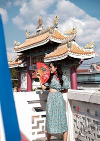 Portrait of woman in blue modern cheongsam holding a red fan at chinese temple 