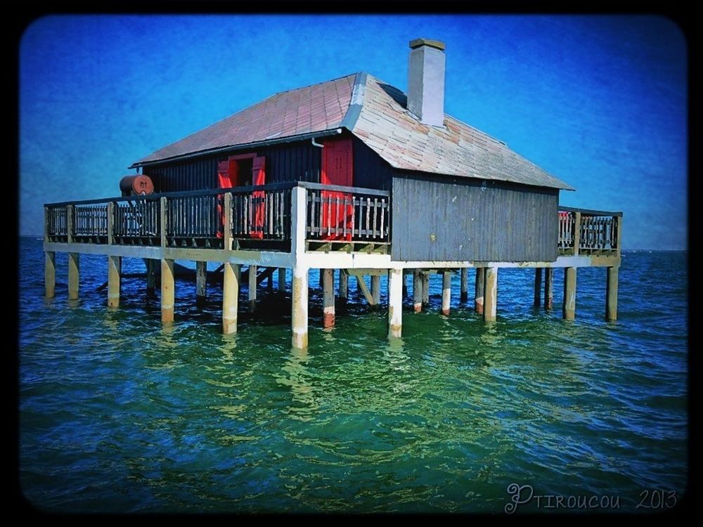 transfer print, water, auto post production filter, built structure, architecture, blue, sea, building exterior, beach, waterfront, sky, day, house, nature, outdoors, clear sky, sunlight, wood - material, tranquility, sand