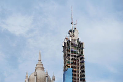 Low angle view of old and new building against cloudy sky