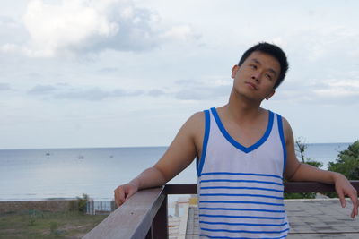 Man looking away while standing by railing against sky