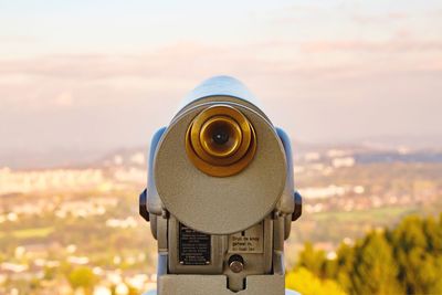 Close-up of coin-operated binoculars by cityscape against sky