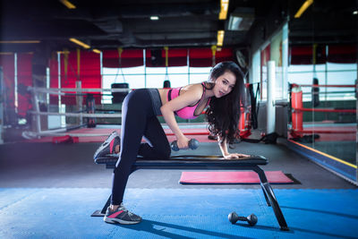 Confident young woman holding dumbbell while exercising in gym