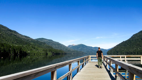 Rear view of man standing on footbridge over lake against sky