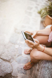 Unrecognizable woman sitting on a stone watching her mobile phone