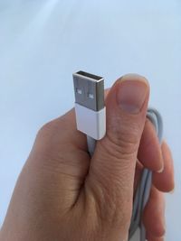 Close-up of hand holding usb cable against white background