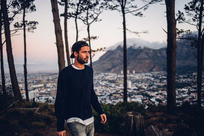 Young man looking away while standing in forest