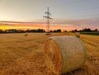 Hay bales on field against sky during sunset