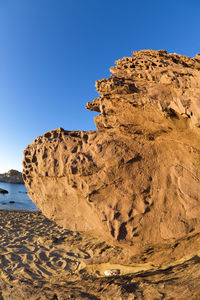 Rock formations on beach against clear blue sky