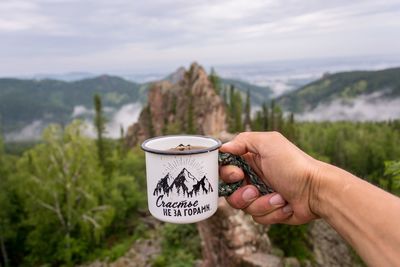 Midsection of person holding cup against mountain range