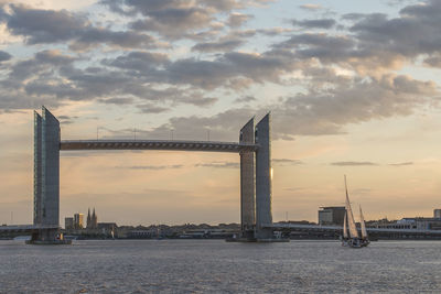 Bridge over river in city against cloudy sky