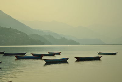 Boats in lake against sky during sunset