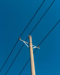 Low angle view of telephone pole against clear blue sky