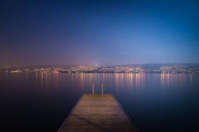 Illuminated city by sea against sky at night