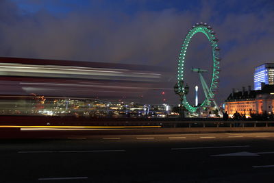 Illuminated ferris wheel by city against sky at night