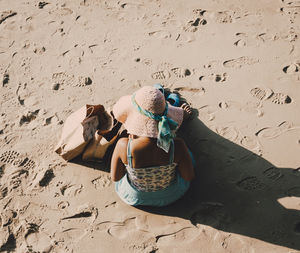 High angle view of woman sitting at sandy beach on sunny day