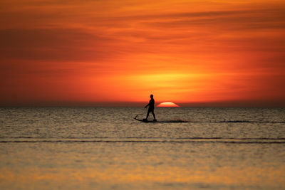 Silhouette person in sea against sky during sunset