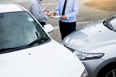 Midsection of men discussing while standing by cars