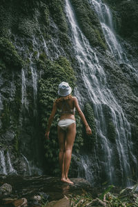 Rear view of woman standing against waterfall in forest