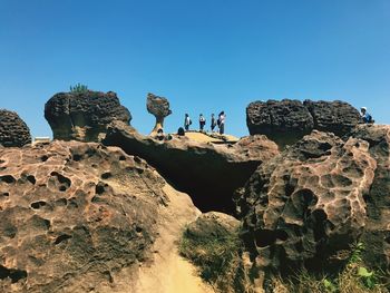 People standing on rock formation against clear blue sky