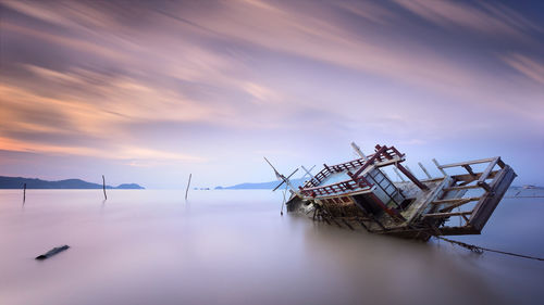 Abandoned ship in sea against sky during sunset