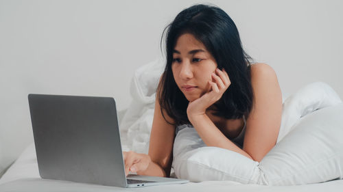 Young woman using mobile phone while sitting on bed