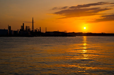 Silhouette buildings by sea against orange sky