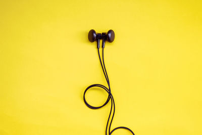 High angle view of in-ear headphones on yellow background