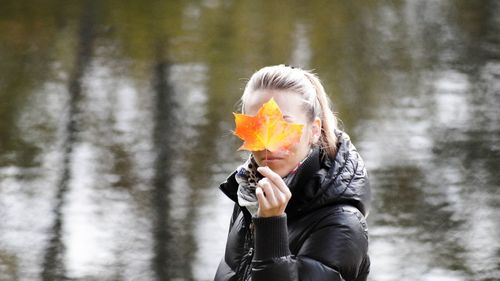 Young woman holding maple leaf while standing by lake