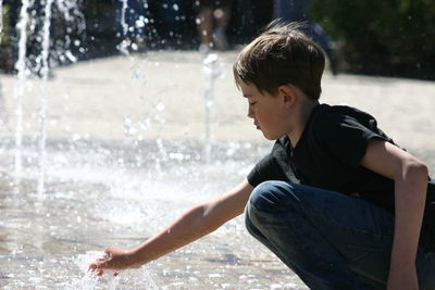 Side view of boy playing on fountain
